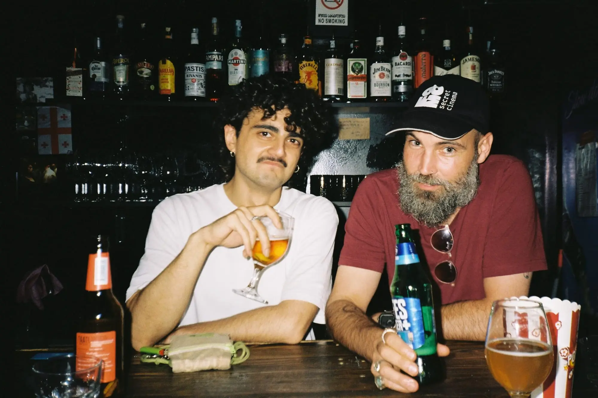 David and Murat at the FOMO bar, a wall of bottles lit behind them