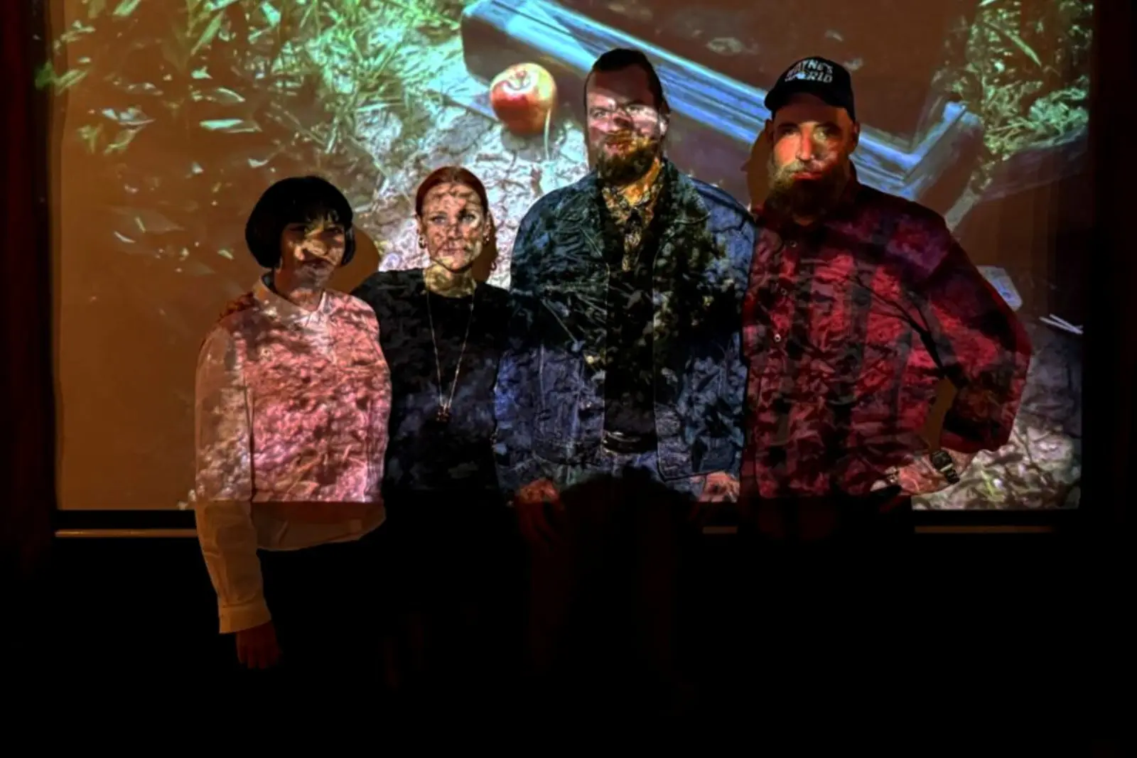 Four people standing in front of the cinema screen, the projected film falling across them