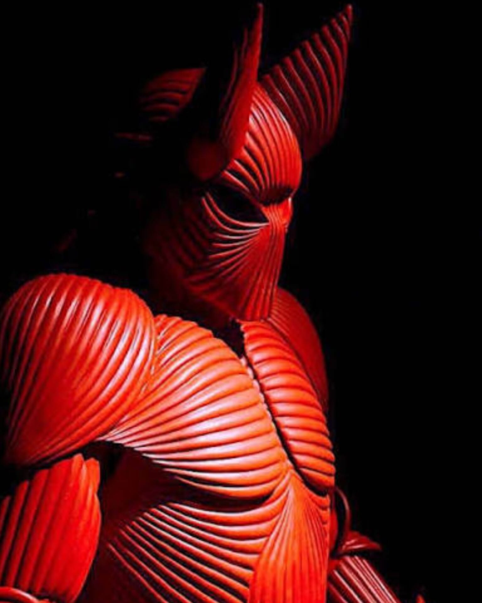 A red pleated sculpture lit against black